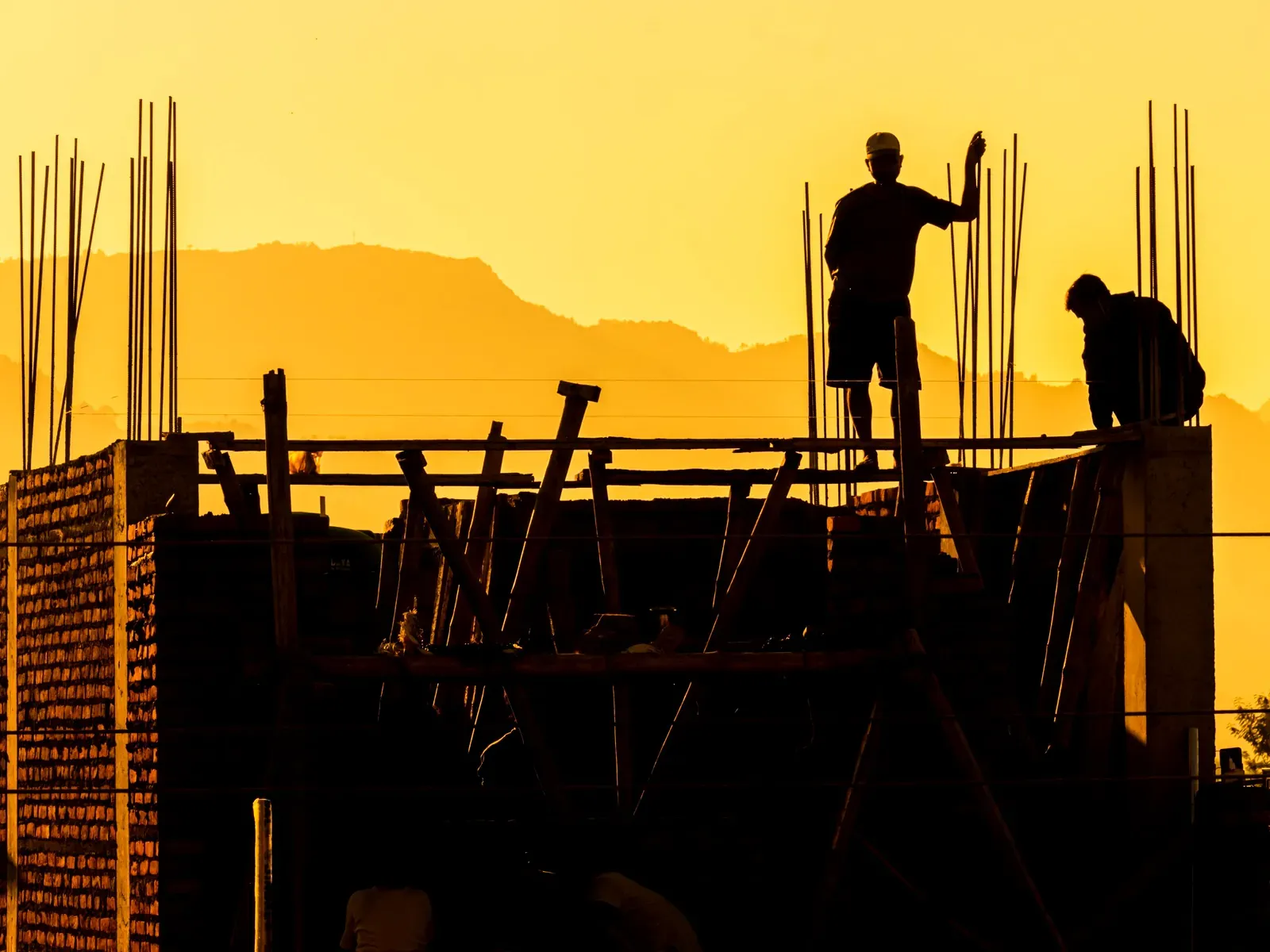 Two builders in silhouette on a building frame against an orange sky